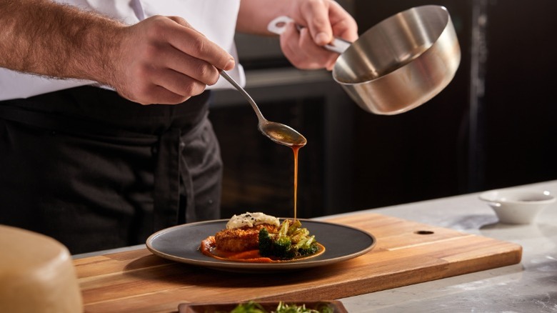 A chef drizzles sauce over a grey plate of food