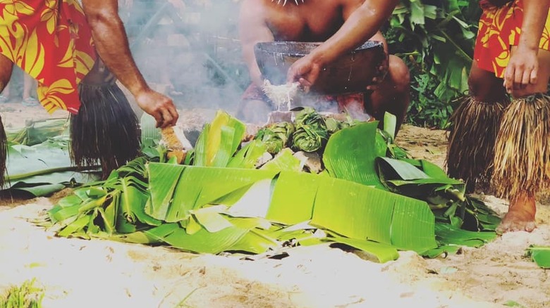 Staff places food in ground oven