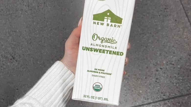 A hand holding a box of New Barn almond milk