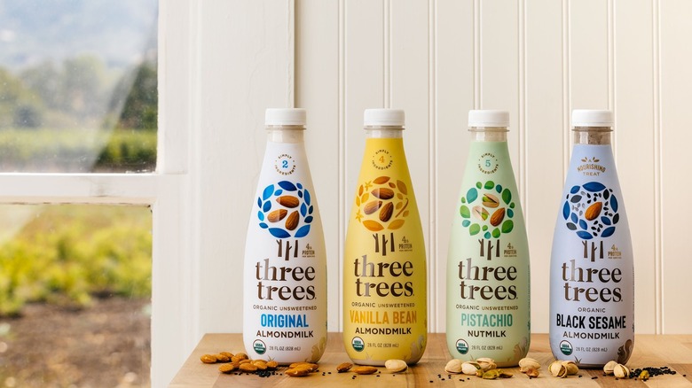 A table of Three trees nut milk bottles surrounded by nuts