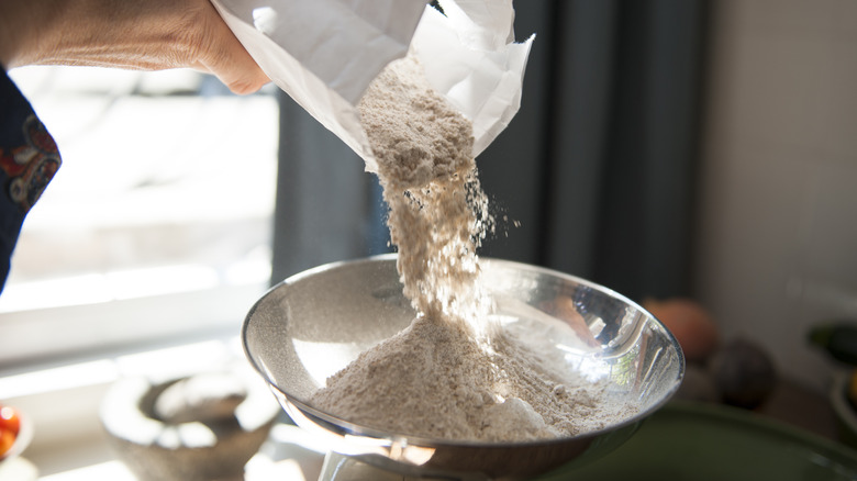 A hand pouring flour out of a bag into a stainless steel bowl