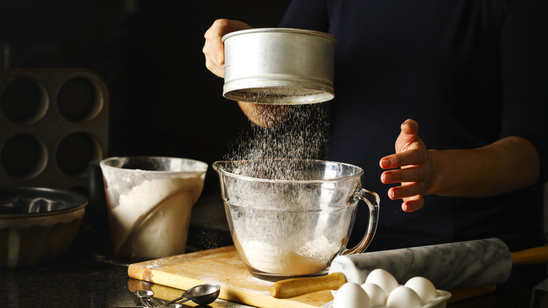 Hands sifting flour through a sieve into a glass measuring cup