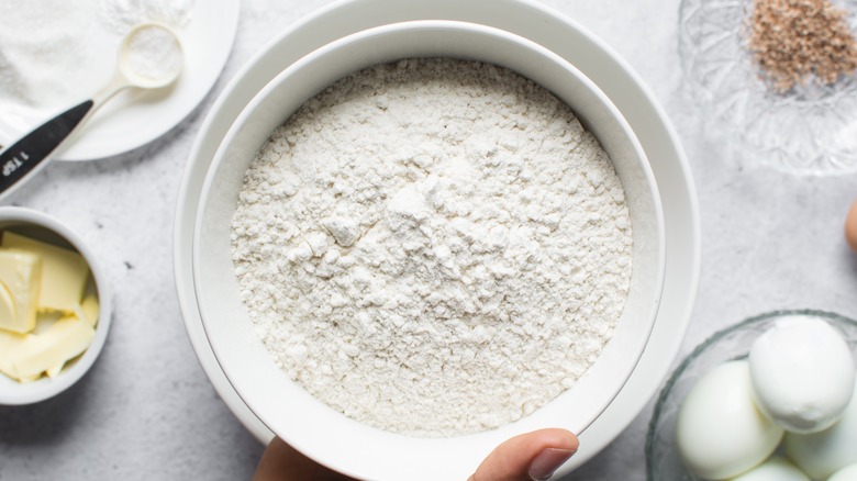 Bleached flour in a white bowl beside eggs and butter