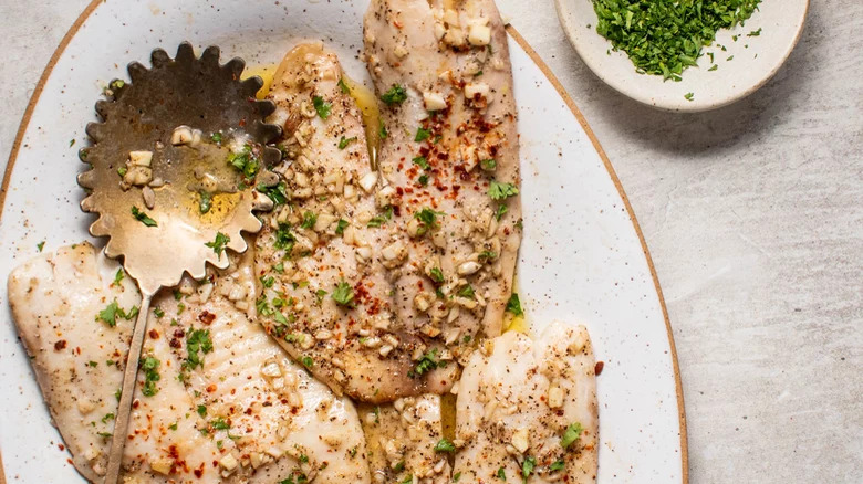 baked tilapia with herbs on white plate