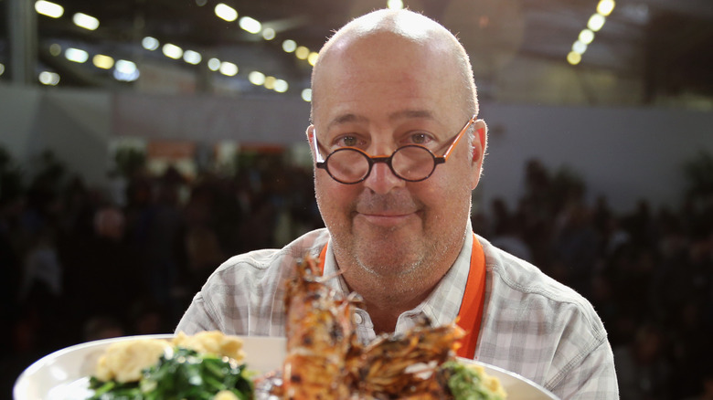 Andrew Zimmern wearing glasses and holding food