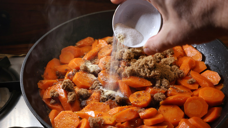 pouring small dish of spices into skillet of sliced carrots with brown sugar