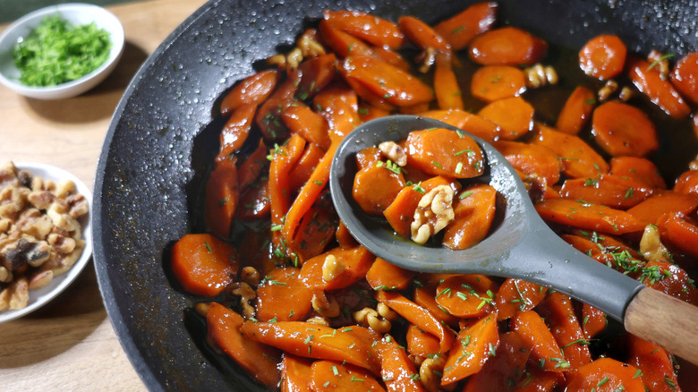 serving spoon full of glazed carrots in skillet of glazed carrots