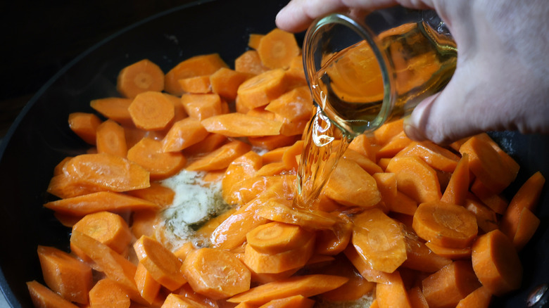 pouring glass of bourbon whiskey into skillet full of carrots