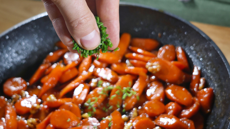 sprinkling chopped chives over skillet of glazed carrots