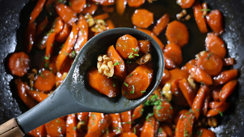 serving spoon of glazed carrots and walnuts over skillet full of glazed carrots