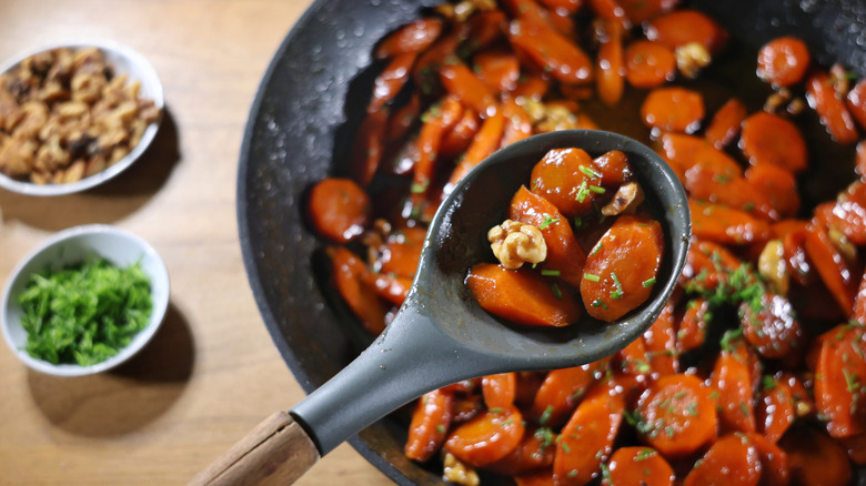 serving spoon of glazed carrots and walnuts over skillet full of glazed carrots