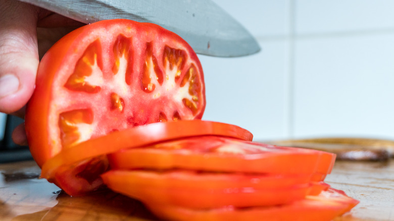 Person slicing a red tomato with a knife