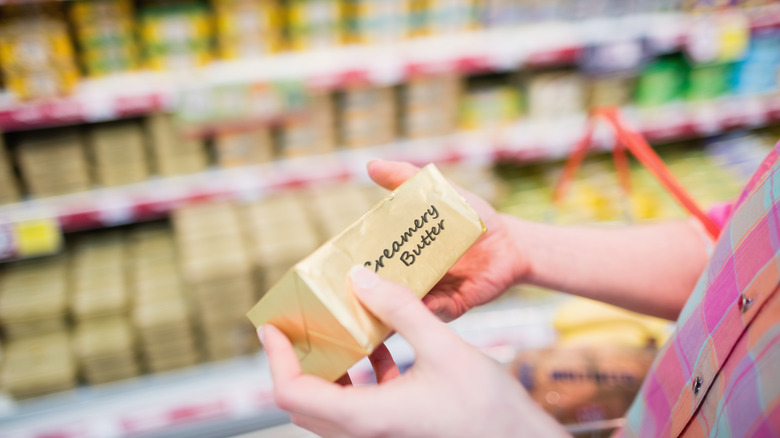 in the hands of a women is creamy butter while out of focus is the butter aisle