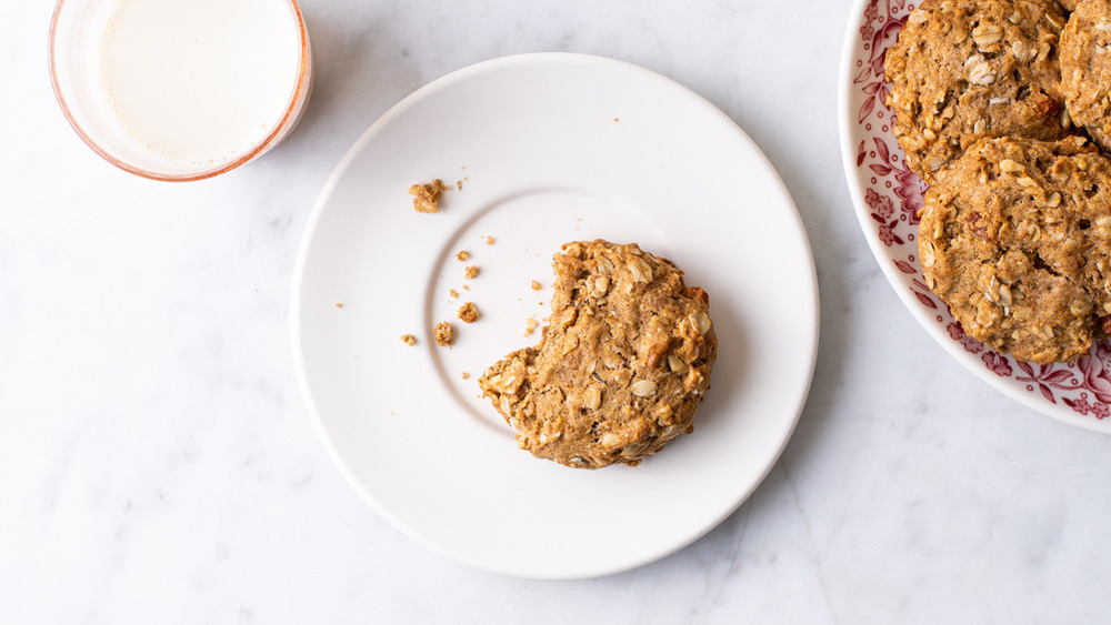 no-bake healthy oatmeal cookies on a plate next to a cookie with a bit out of it on a white plate near a glass of milk on a white counter