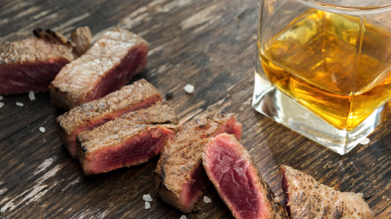 A cut steak and glass of whiskey paired together