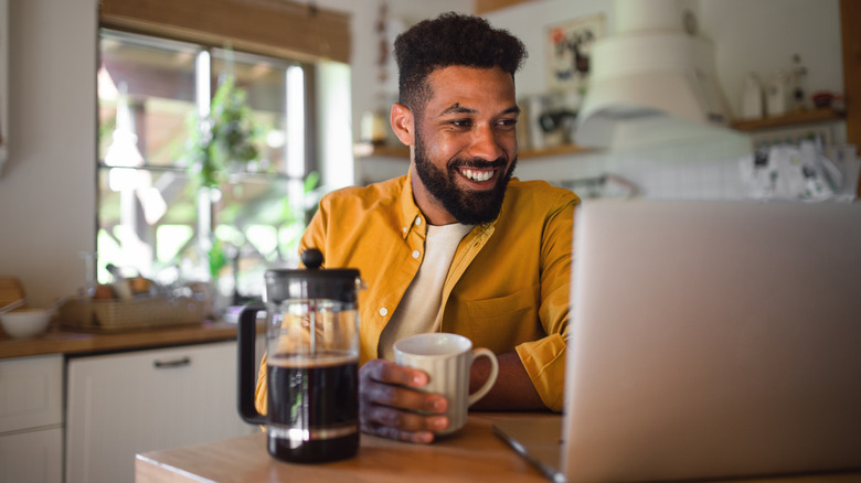 Man looks at computer and drinks coffee