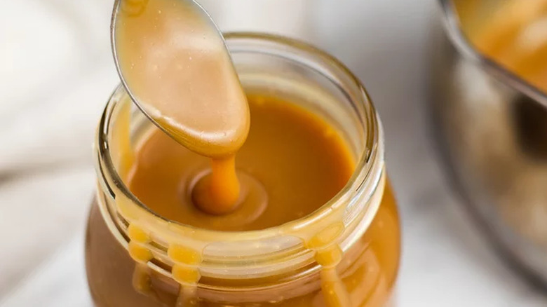 Caramel sauce inside glass jar and dripping from spoon.