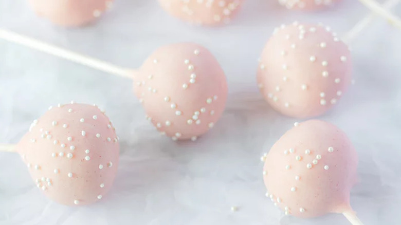 Cake pops with pink coating and white sprinkles.