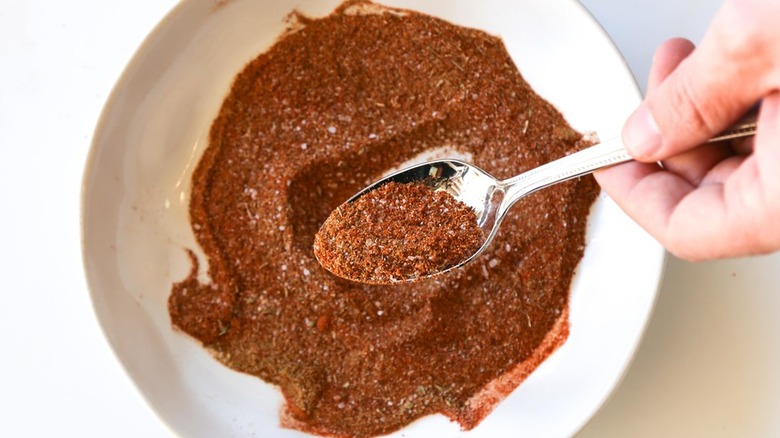 Bowl of taco seasoning blend with hand and spoon.