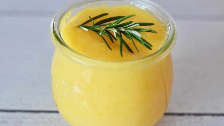 Small glass jar of thick lemon curd with rosemary sprig.
