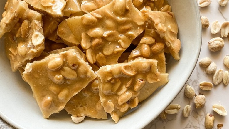 Pieces of peanut brittle candy in white bowl.