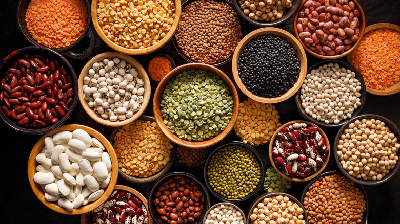 Legumes, a set consisting of different types of beans, lentils and peas on a black background, top view. 