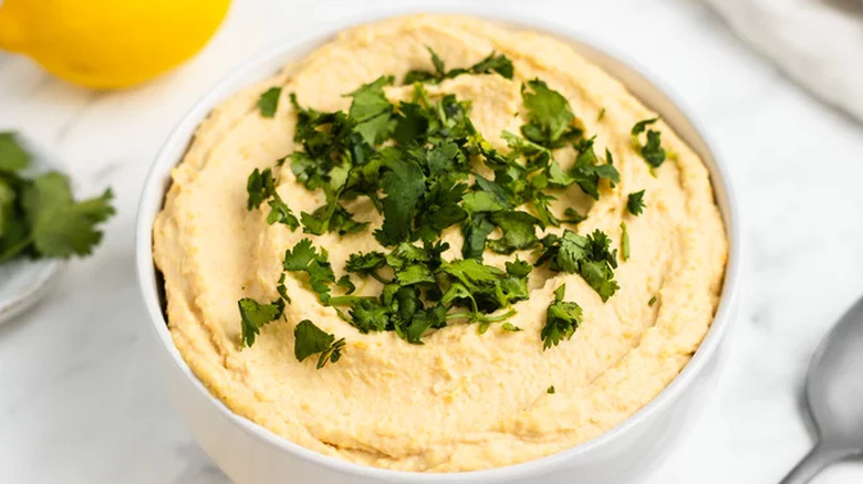 White bowl of lemon hummus with parsley