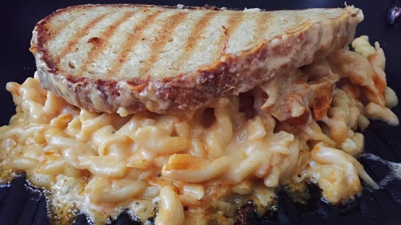 Grilled sandwich with mac and cheese spilling out of it. 