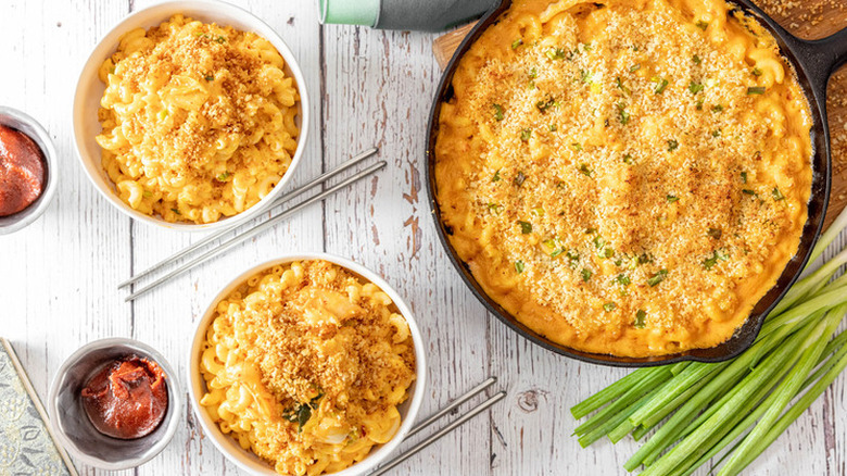 Iron skillet and bowls of macaroni and cheese with breadcrumb topping. 