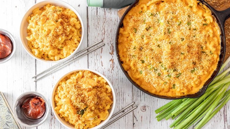 Iron skillet and bowls of macaroni and cheese with breadcrumb topping.