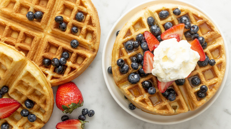 golden brown belgian waffles topped with fresh blueberries and strawberries, whipped cream, and maple syrup.