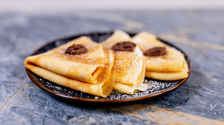 Three folded crepes on a plate dusted with powdered sugar