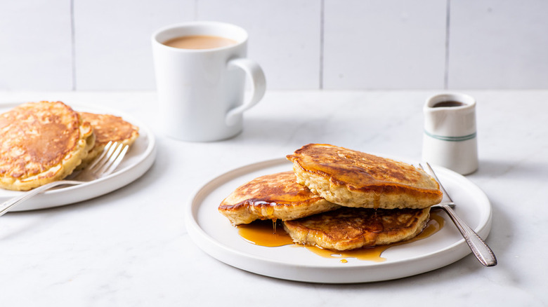 A stack of oatmeal pancakes on a white plate with maple syrup on it