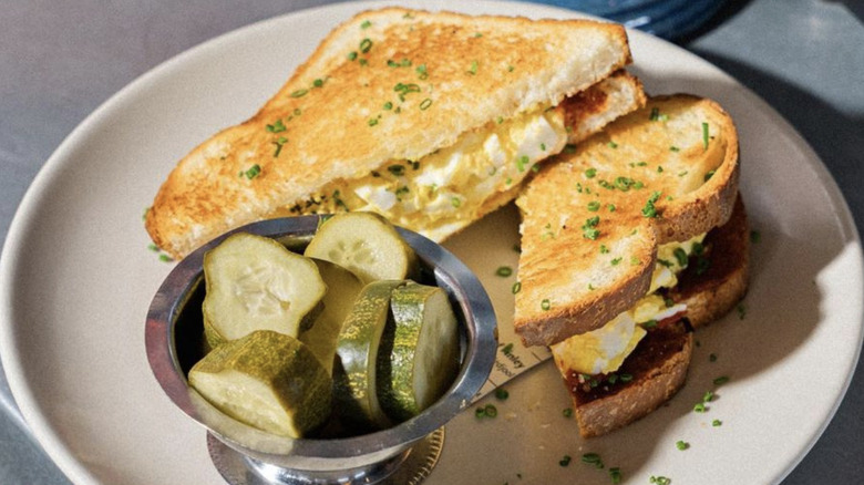 Egg salad sandwich with dish of pickles