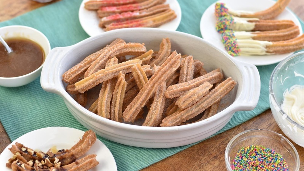 homemade churros with icing, chocolate sauce and nuts