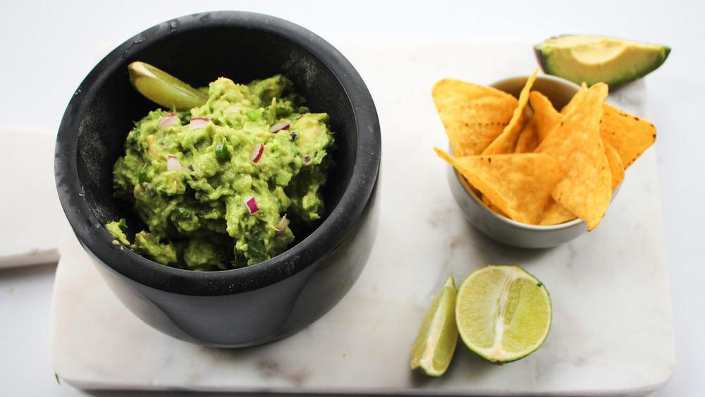 A bowl of guacamole, with chips and lime slices.