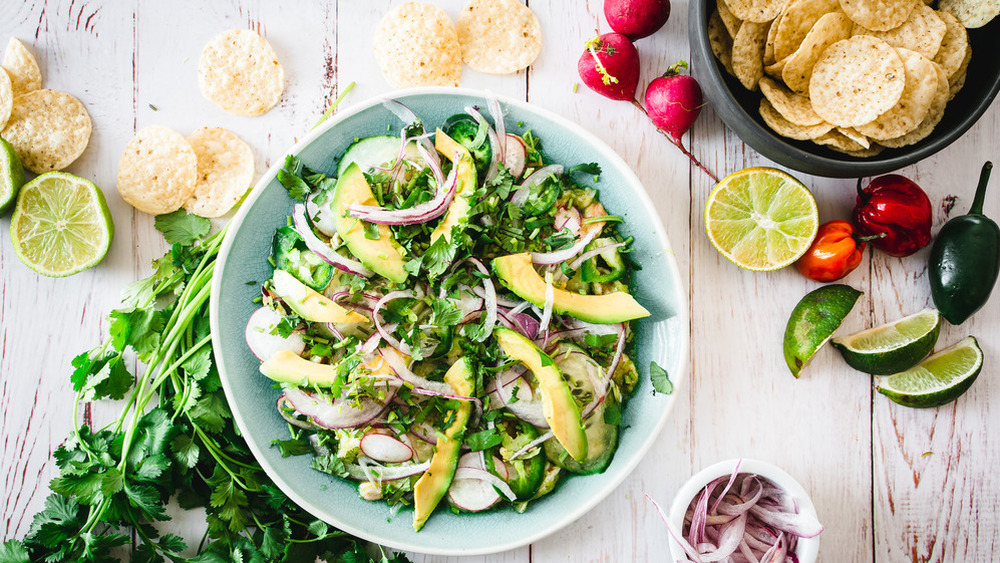 A bowl of aguachile surrounded by chips, limes, and radishes.