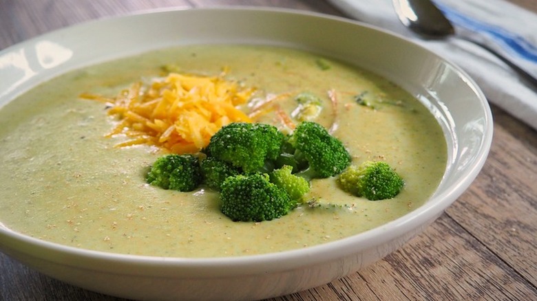 Shallow bowl of broccoli soup with broccoli florets and cheese.