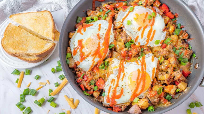 Crumbled sausage, peppers, and fried eggs in a skillet.