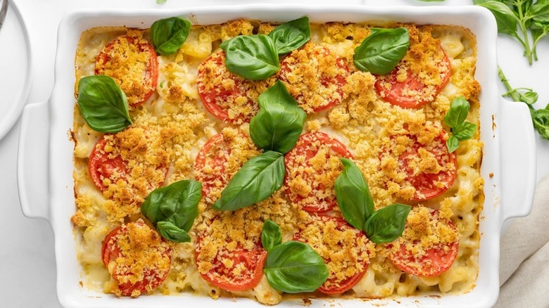 White baking dish with pasta, cheese, basil, and tomatoes.