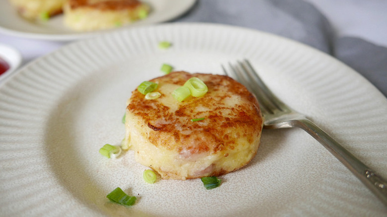 Round potato cake on a plate with sliced scallions.