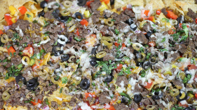 Nachos with ground beef, olives, cheese, and herbs.