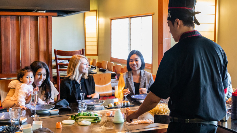 A chef preparing food on a hibachi grill in front of guests