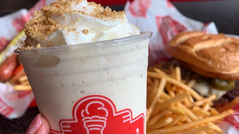 close up of a milkshake with fries and a burger in the background