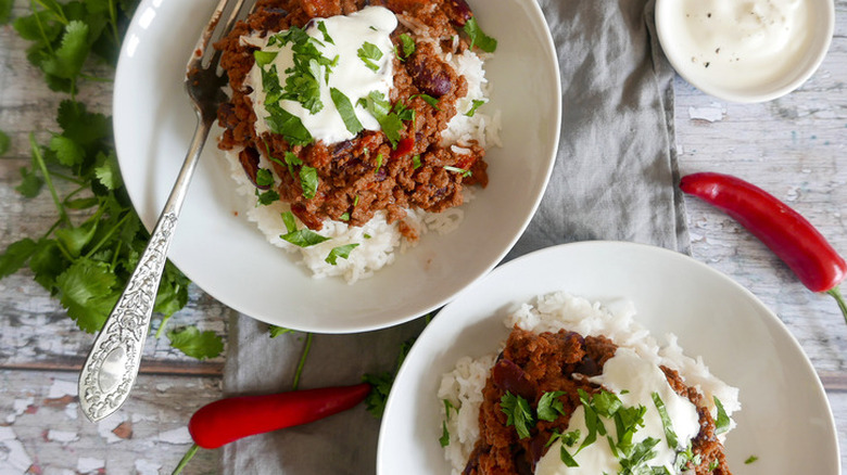 Beef chili over white rice in two white bowls.