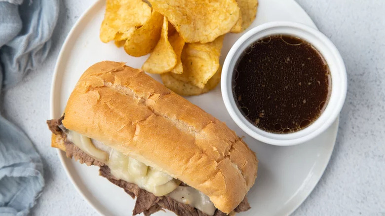 Beef and cheese sandwich with bowl of au jus. 