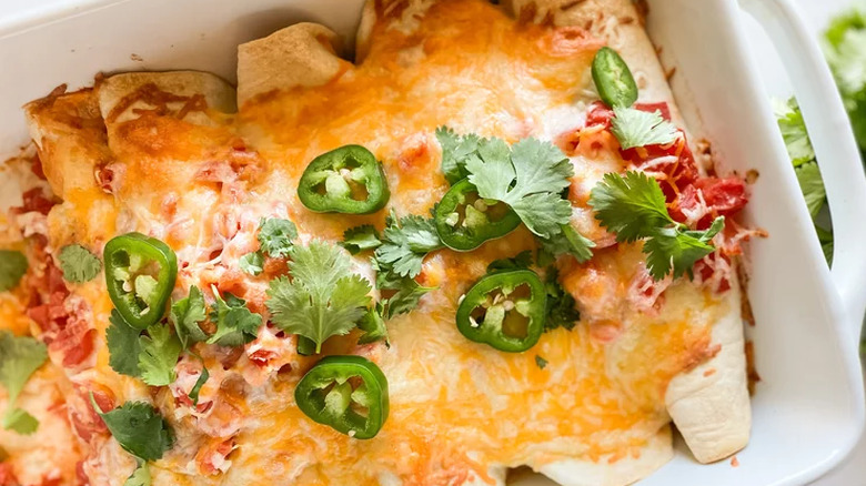 Rolled tortillas with melted cheese in a casserole dish.