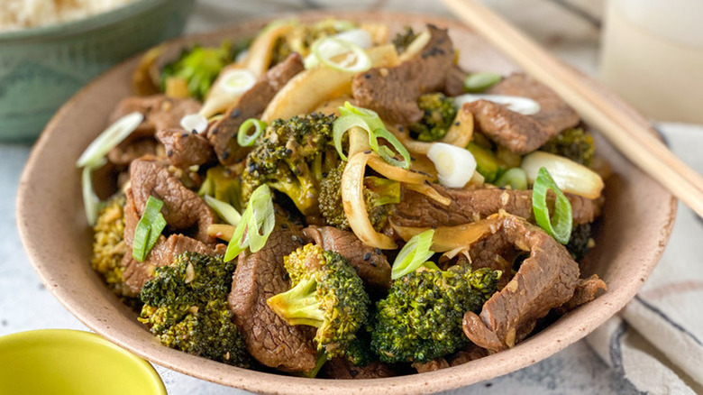 Beef and broccoli with sliced onions in a brown bowl.