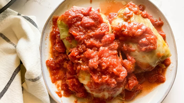 Filled cabbage rolls on plate with tomato sauce.