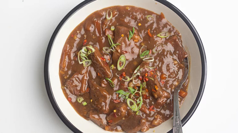 Pieces of beef in gravy in a large white bowl. 